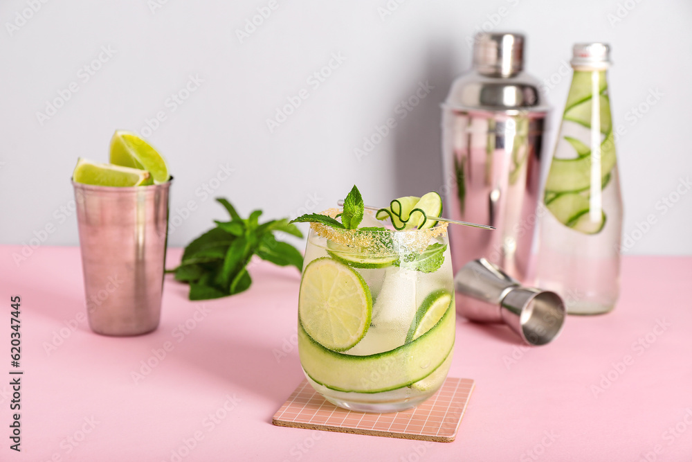 Glass of cucumber mojito with bartender tools on pink background