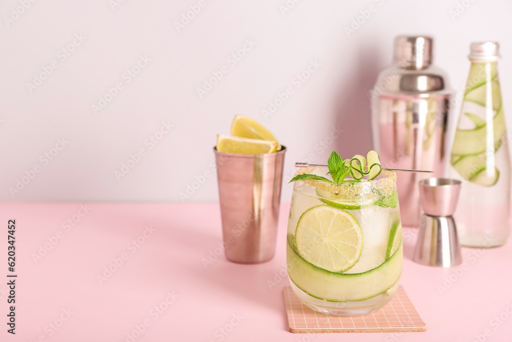 Glass of cucumber mojito with bartender tools on pink background