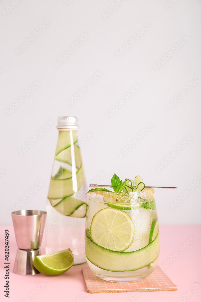 Glass of cucumber mojito with jigger on pink background