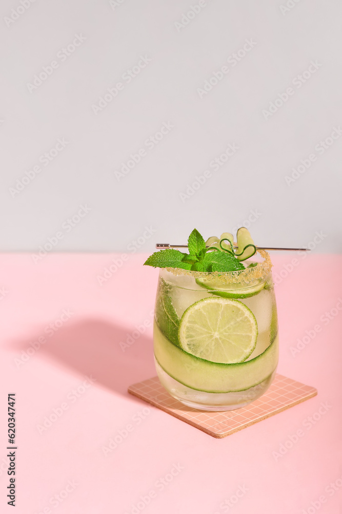 Glass of mojito with cucumber, lime and mint on pink background