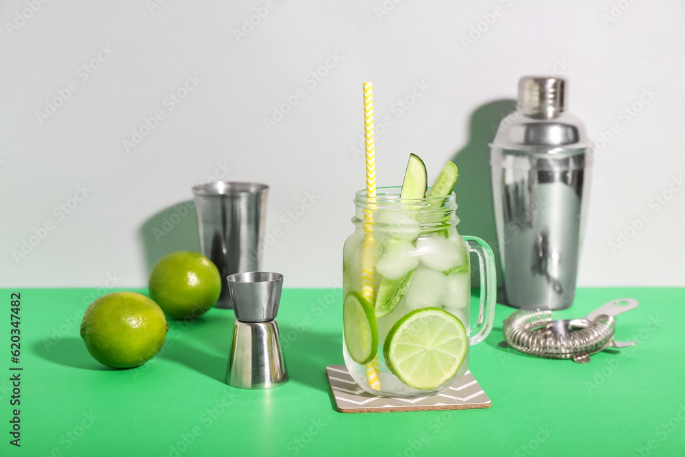 Mojito cocktail in glass jar with bartender tools on color background