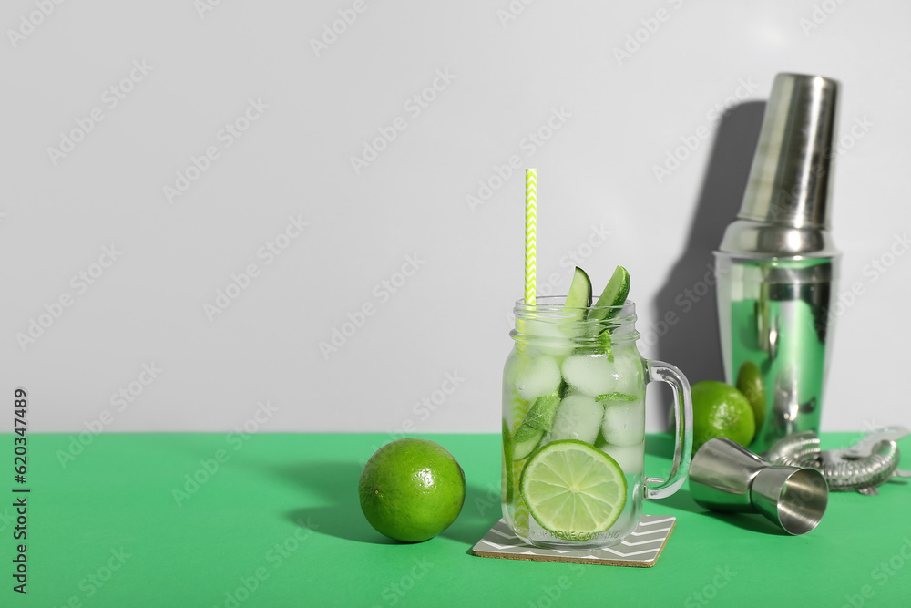 Mojito cocktail in glass jar with bartender tools on color background