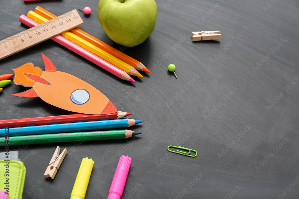 Paper rocket with school stationery and apple on black background