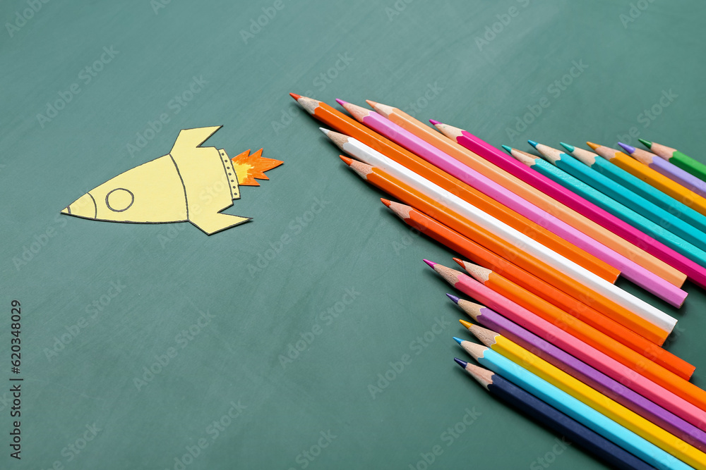 Pencils with paper rocket on green background