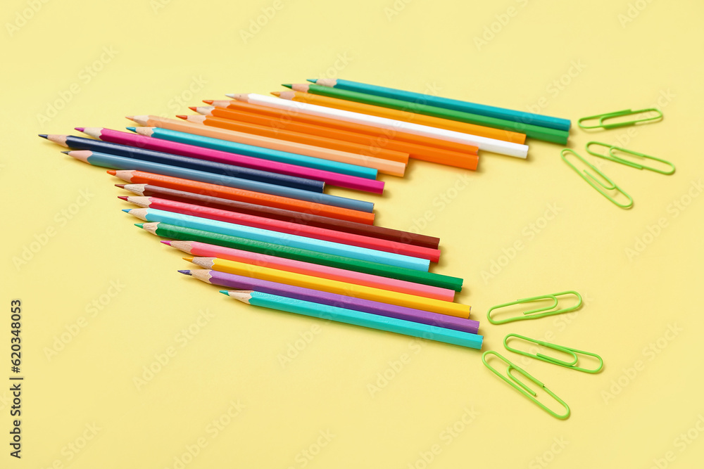 Pencils and paper clips in shape of rocket on yellow background