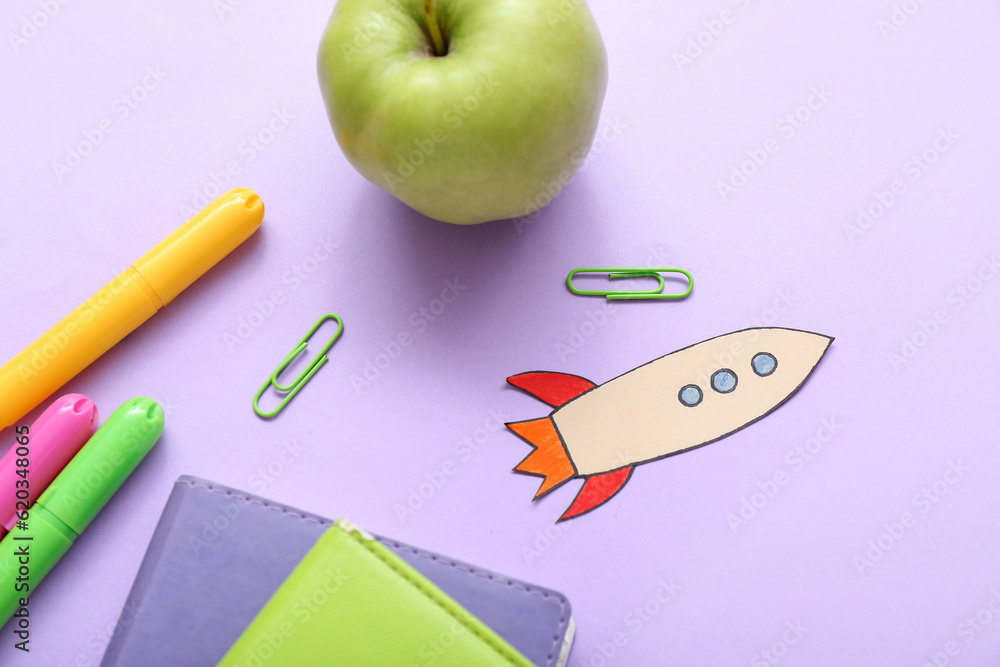 Paper rocket with school stationery and apple on purple background