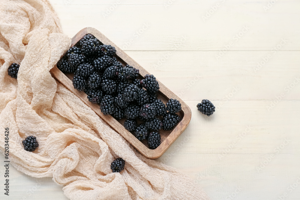 Board with fresh blackberry on light wooden background