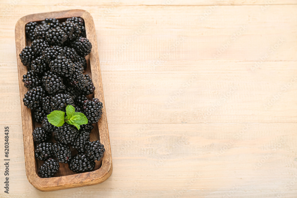 Board with fresh blackberry on light wooden background