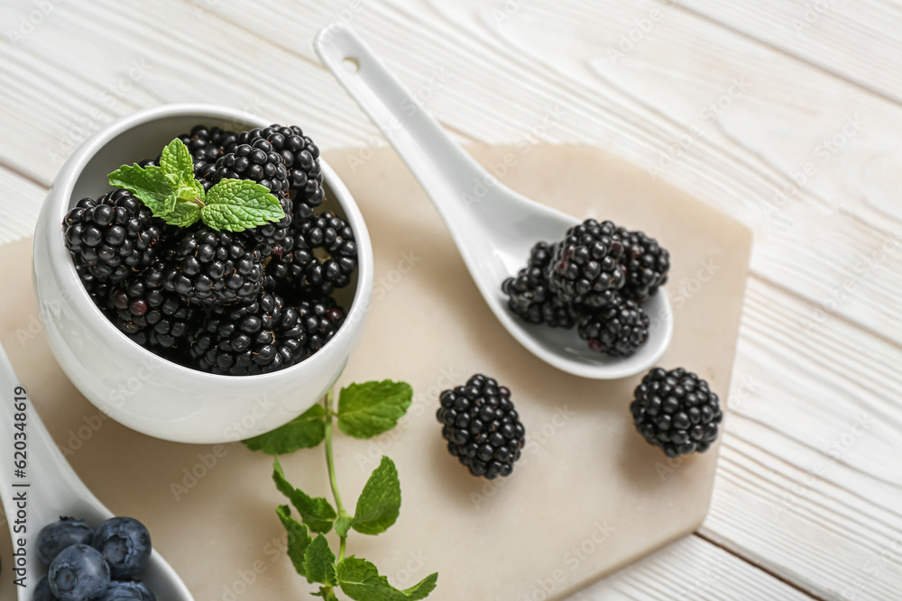 Bowl with fresh blackberry and blueberry on light wooden background, closeup