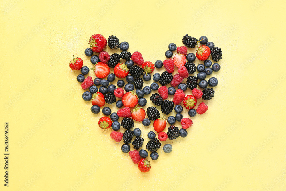 Heart made of different fresh berries on yellow background