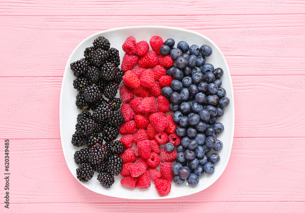 Plate with fresh raspberry, blueberry and blackberry on pink wooden background