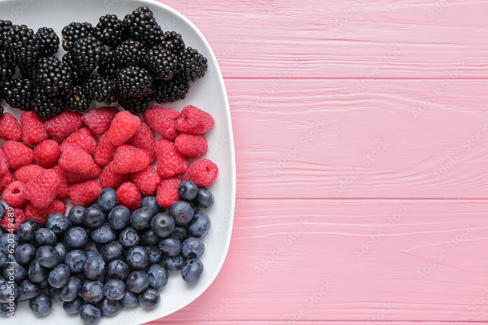 Plate with fresh raspberry, blueberry and blackberry on pink wooden background