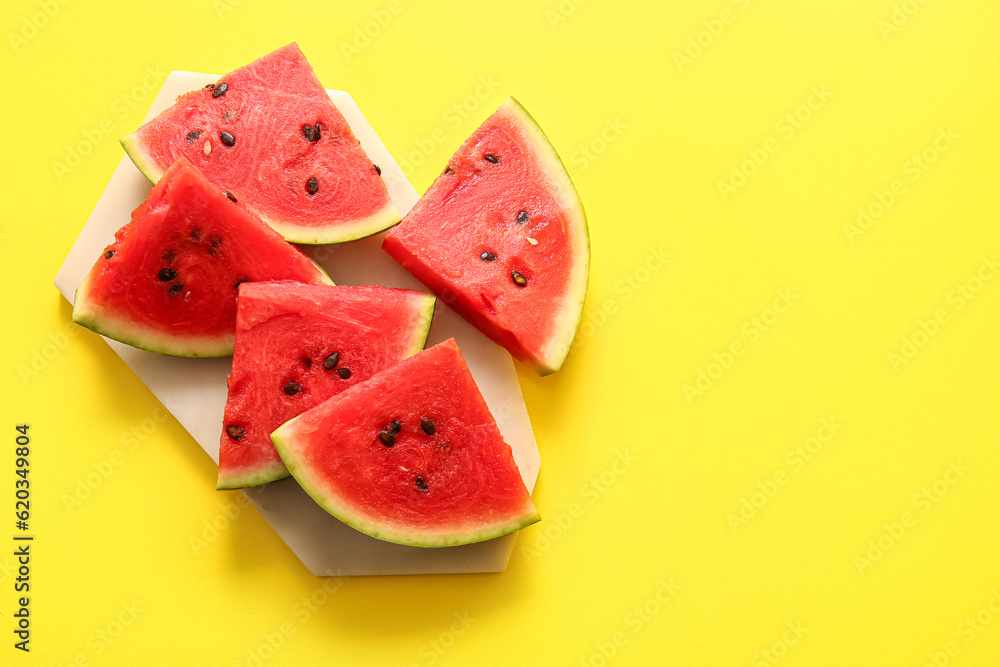 Board with pieces of fresh watermelon on yellow background