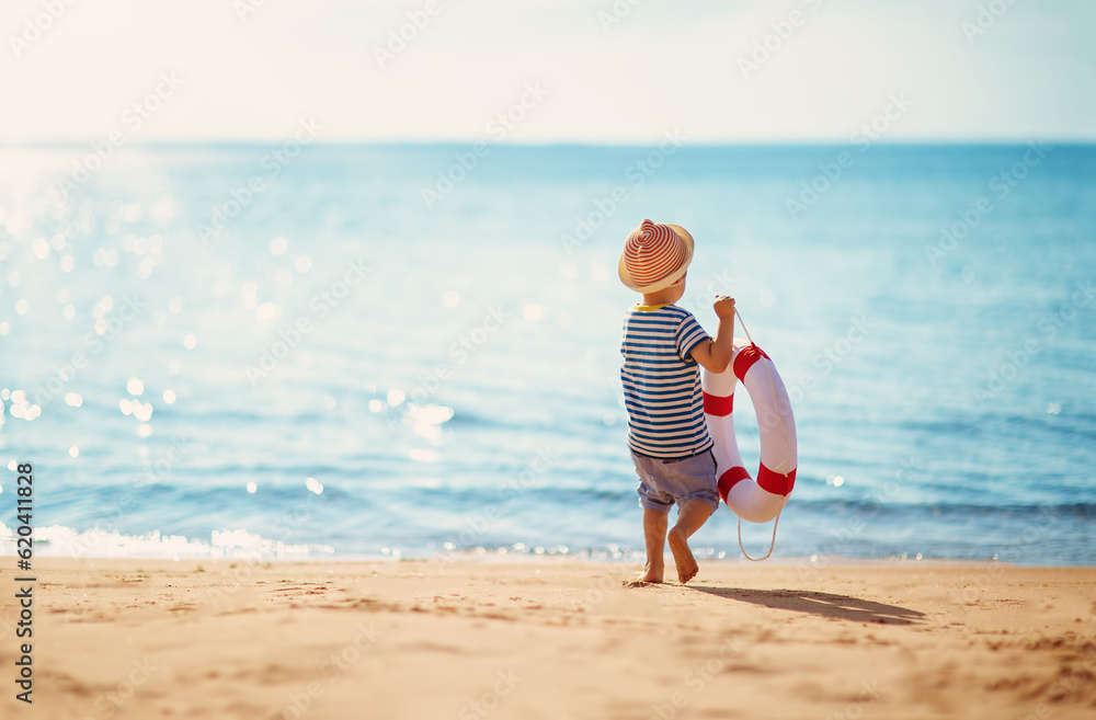 Little boy with lifebuoy in his hands walking alone seaside.