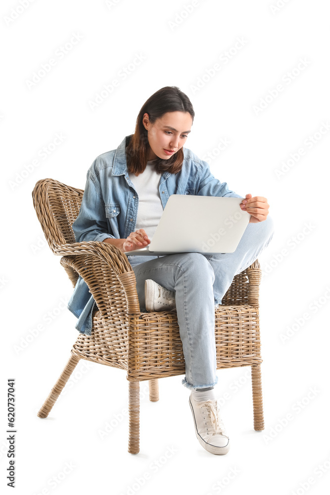 Young woman using laptop in wicker armchair on white background