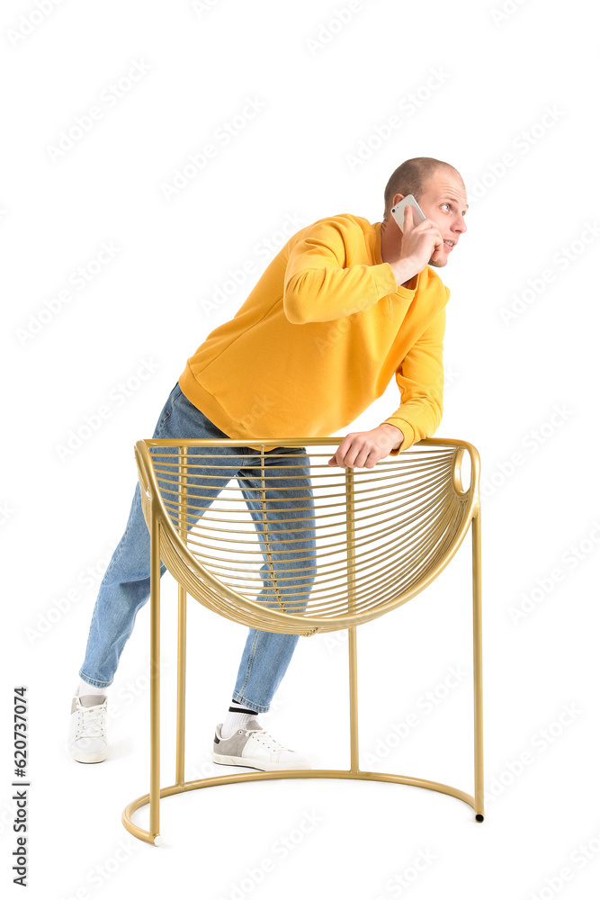 Handsome man talking by mobile phone behind golden armchair on white background