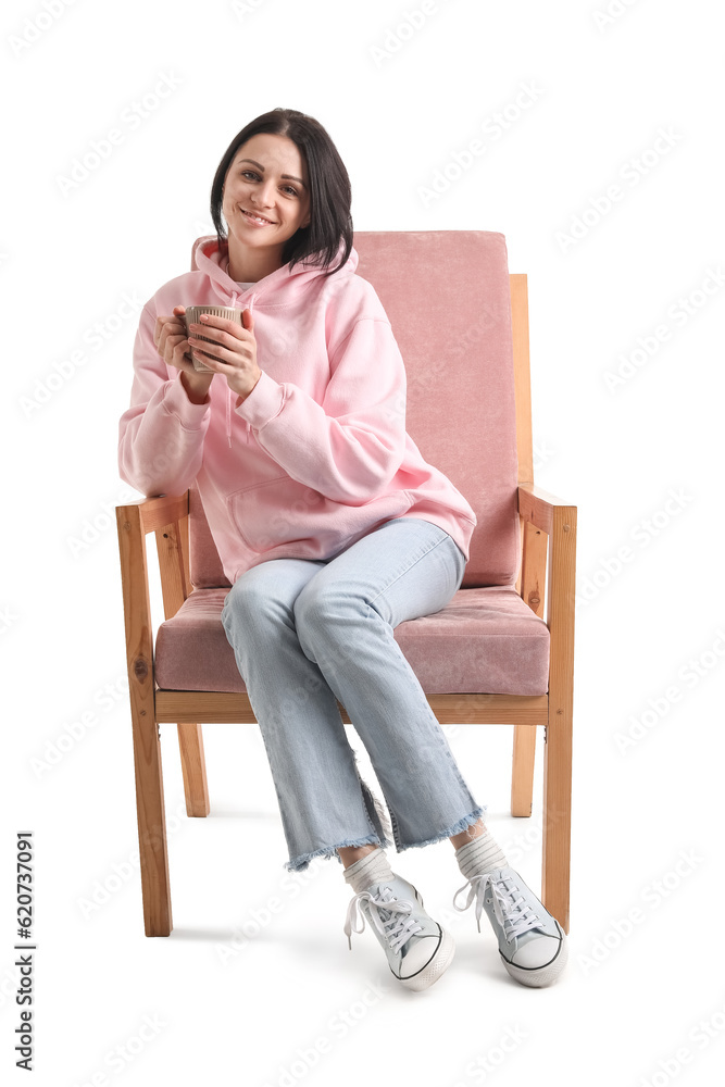 Beautiful woman with cup of tea sitting in pink armchair on white background