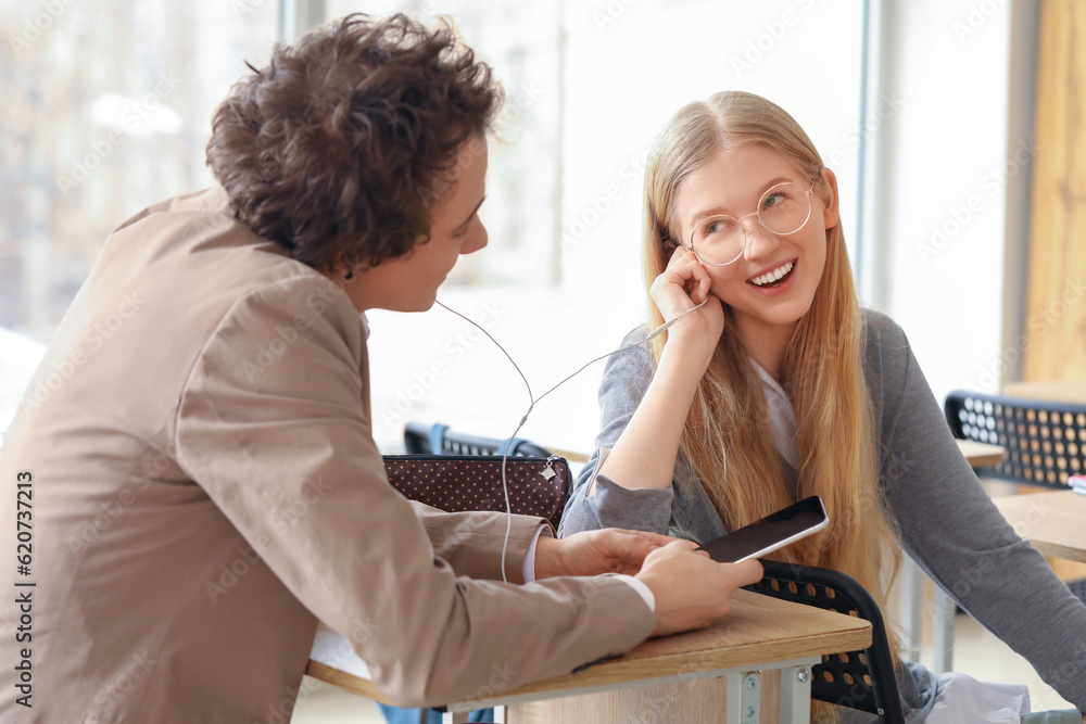 Teenage couple with earphones listening to music in classroom