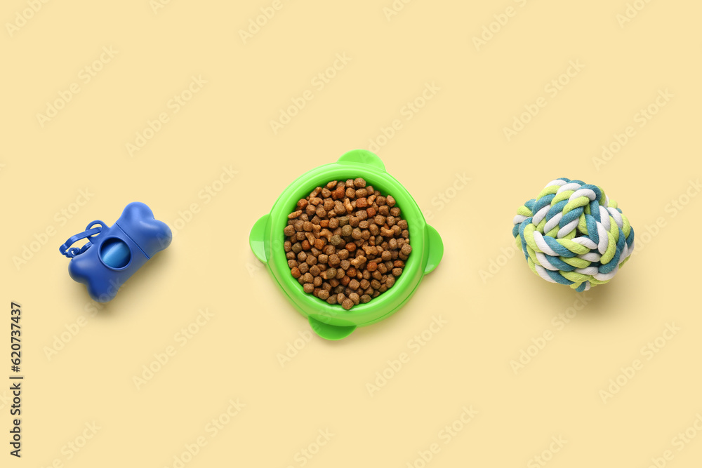 Bowl with dry pet food, toy and waste bags on color background