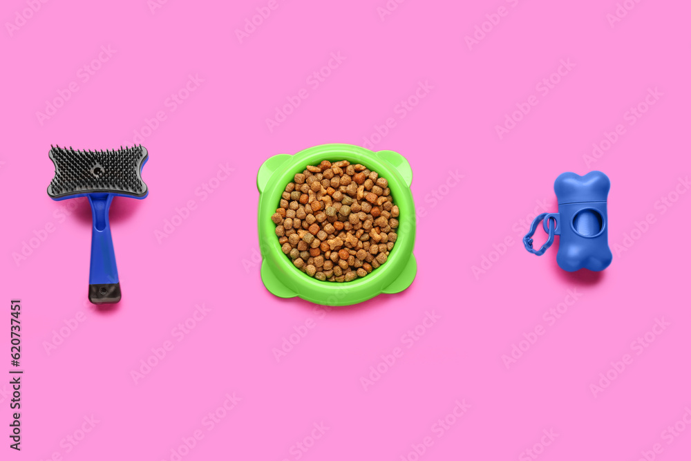 Bowl of dry pet food, waste bags and grooming brush on color background