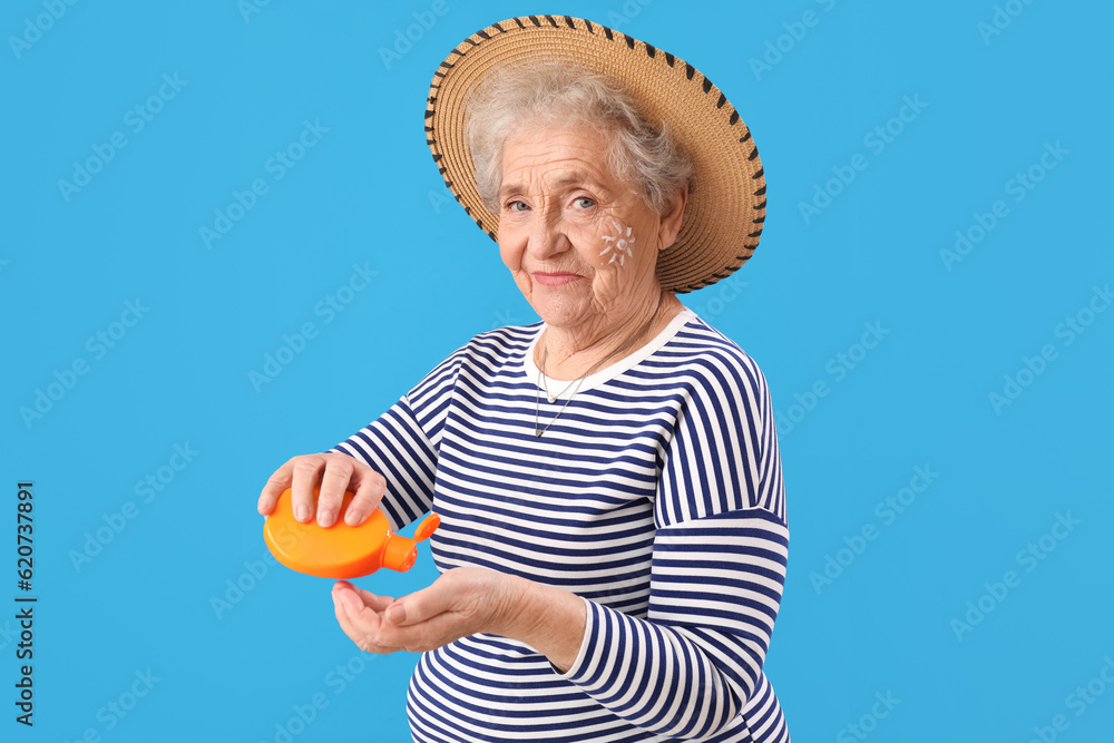 Senior woman applying sunscreen cream on blue background