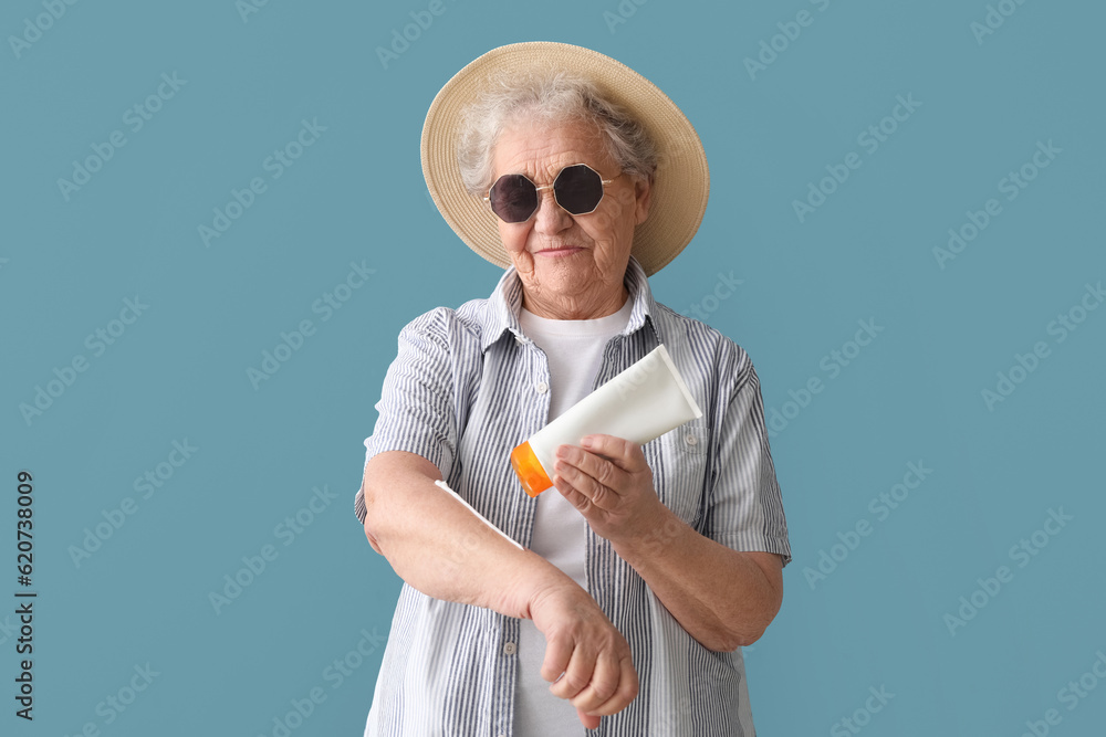 Senior woman applying sunscreen cream on blue background