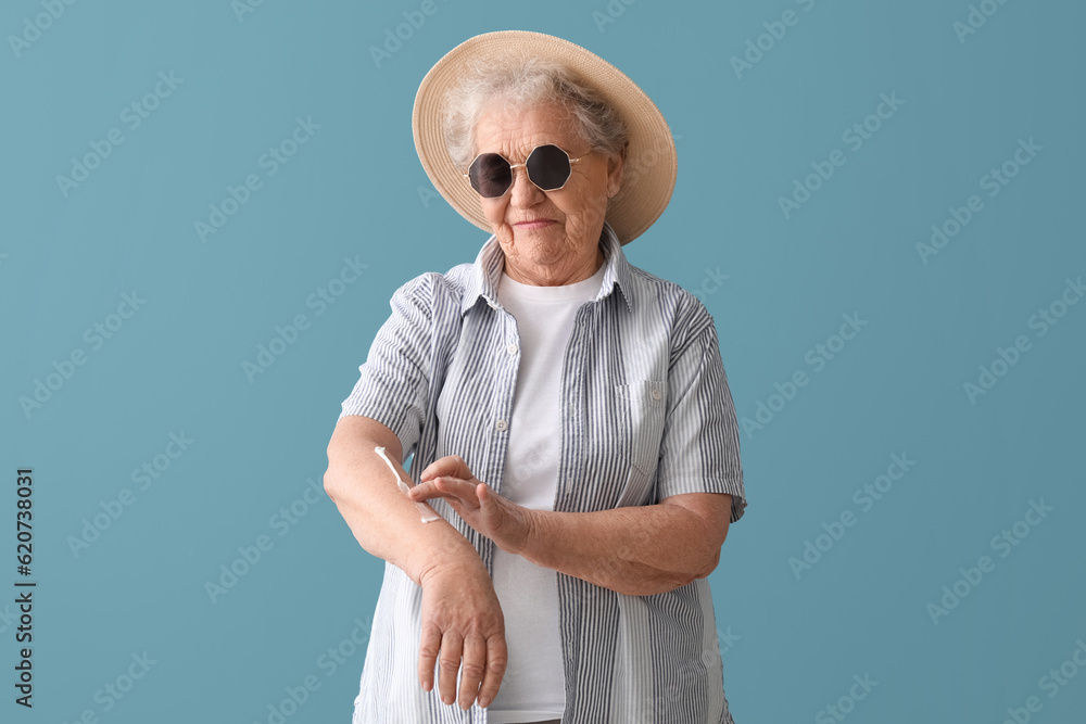 Senior woman applying sunscreen cream on blue background