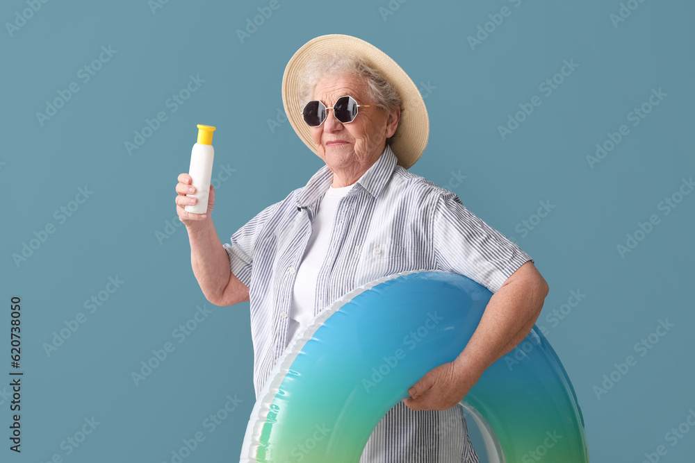 Senior woman with sunscreen cream and inflatable ring on blue background