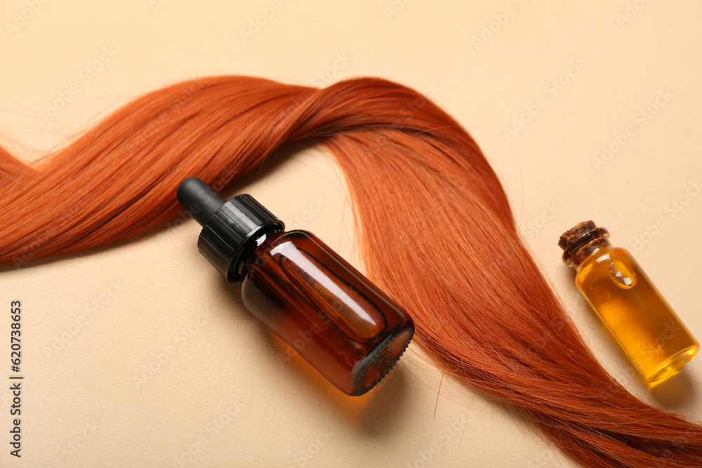 Ginger hair strand and bottles of essential oil on color background, closeup