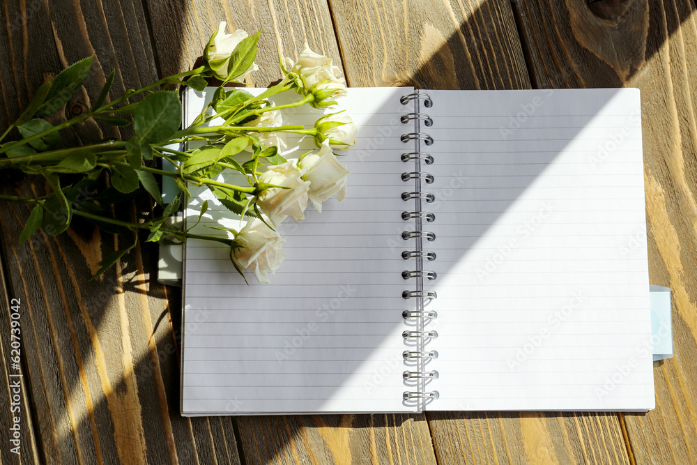 Blank open notebook and beautiful rose flowers on wooden background