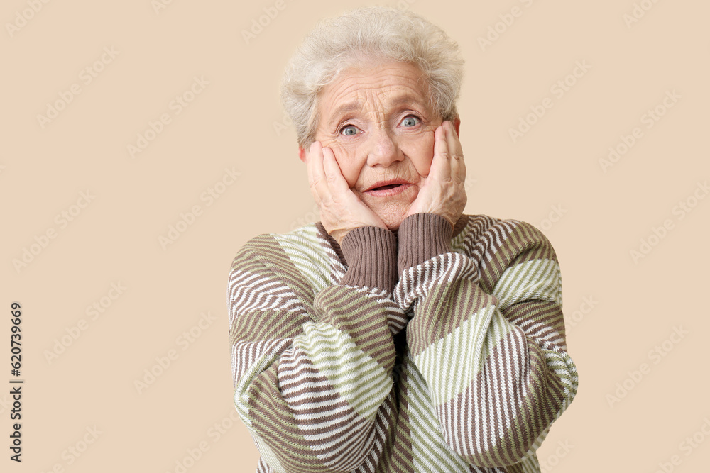 Shocked senior woman on beige background