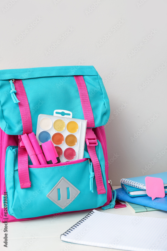 Color school backpack with notebooks, watercolors and markers on white wooden table near wall