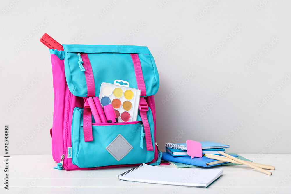 Color school backpack with notebooks, watercolors and markers on white wooden table near wall