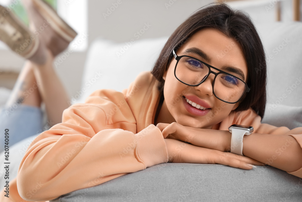 Beautiful young woman wearing glasses while lying on sofa at home