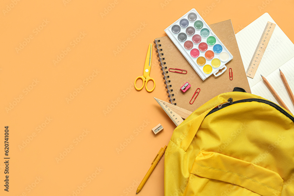 School backpack with paints and stationery on orange background