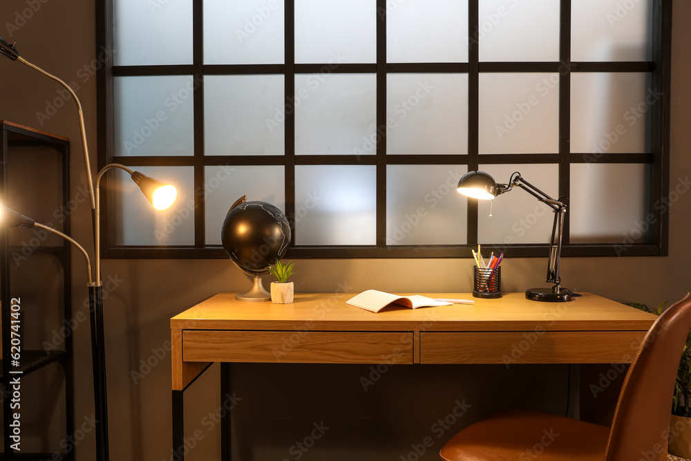 Modern workplace with glowing lamp in interior of dark room