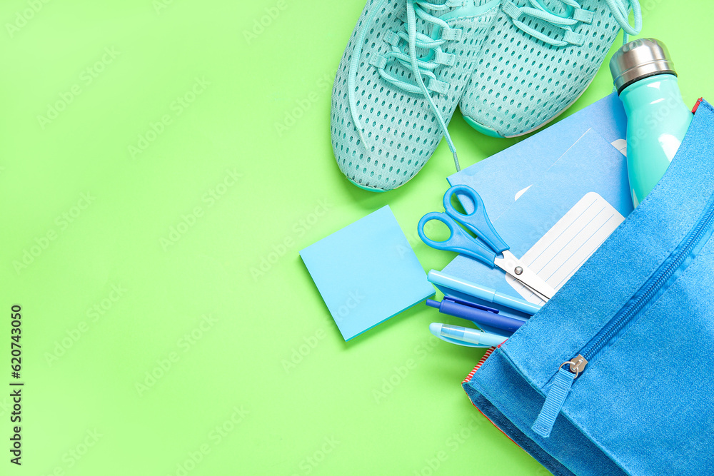 Sneakers with backpack, bottle of water and different stationery on green background