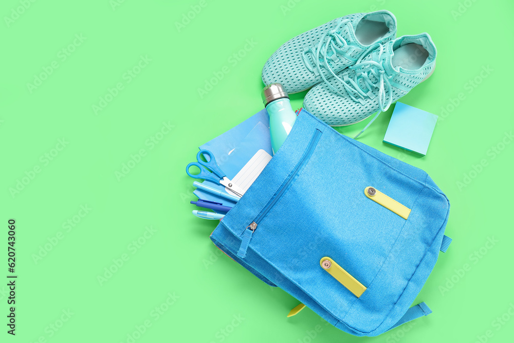 Sneakers with backpack, bottle of water and different stationery on green background