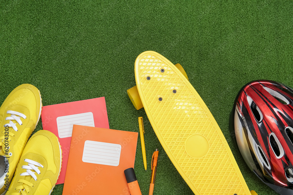 Bike helmet with sneakers, skateboard and different stationery on color background