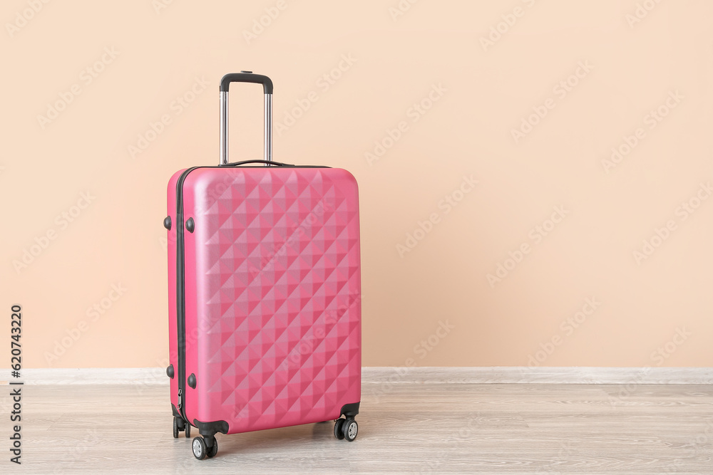 Pink suitcase near pale orange wall. Travel concept