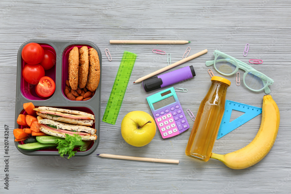 Stationery, eyeglasses and lunch box with tasty food on grey wooden background