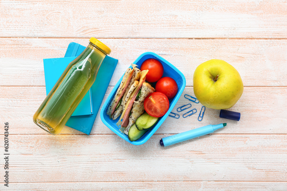 Stationery, drink and lunch box with tasty food on light wooden background