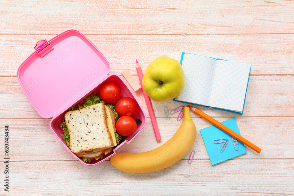 Stationery and lunch box with tasty food on light wooden background