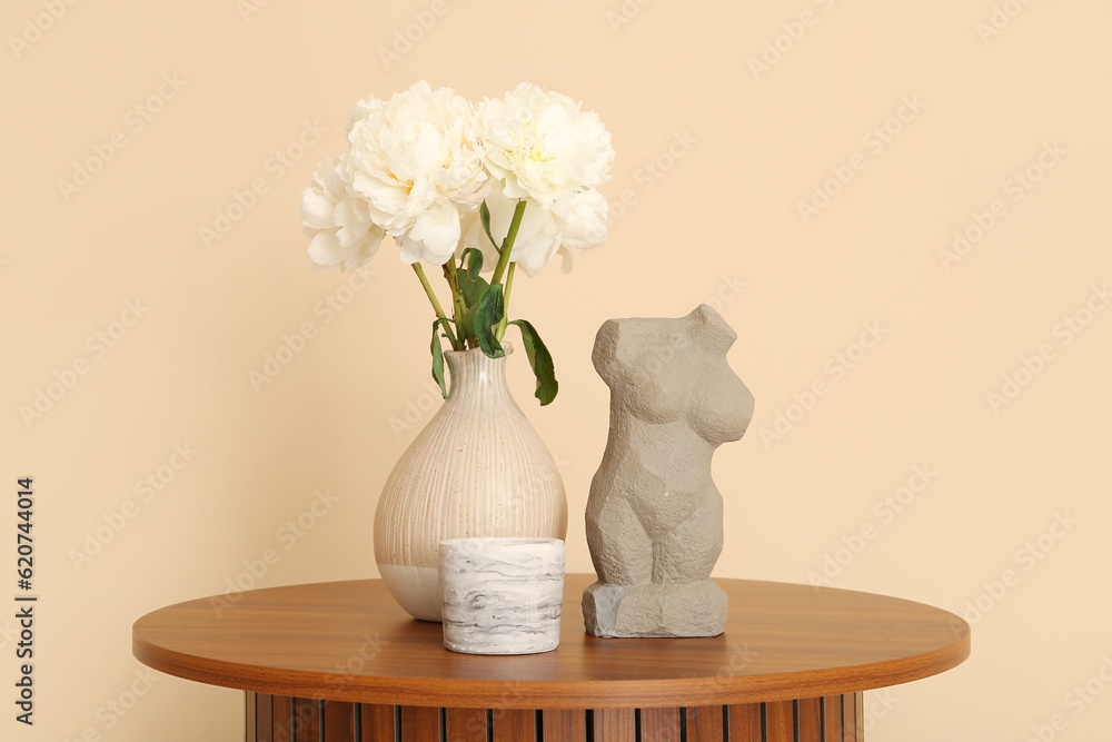 Vase of white peonies and figurine on coffee table near beige wall