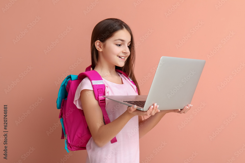 Little girl with backpack using laptop on pink background