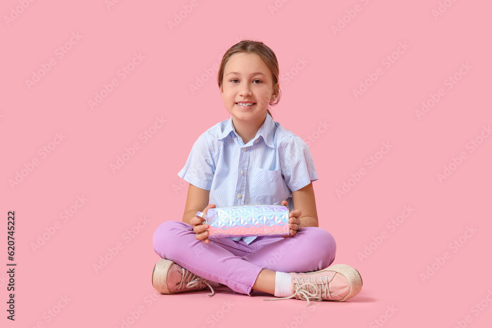 Little girl with pencil case sitting on pink background