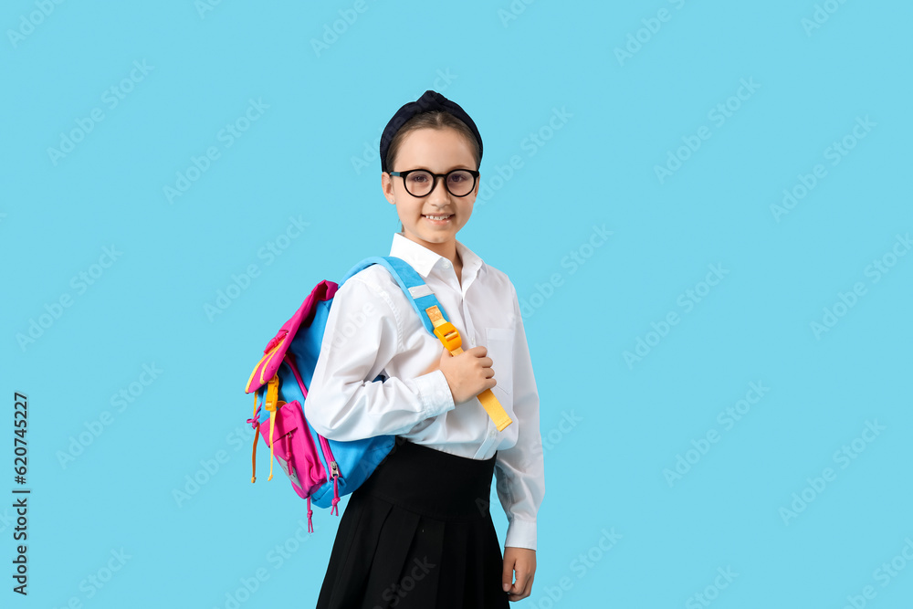 Little schoolgirl with backpack on blue background