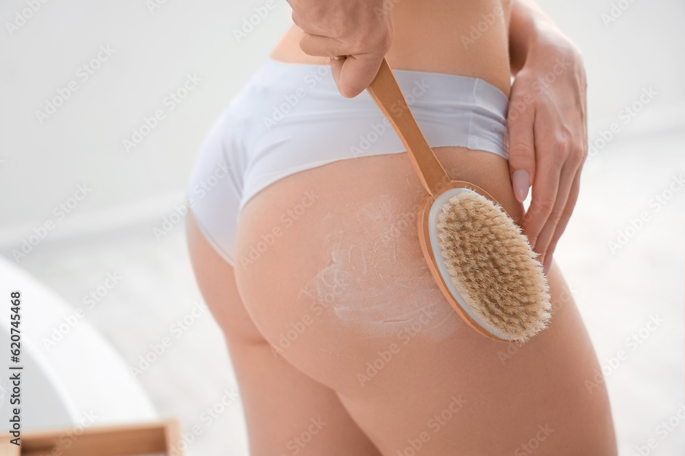 Young woman massaging her buttocks with anti-cellulite brush in bathroom, closeup