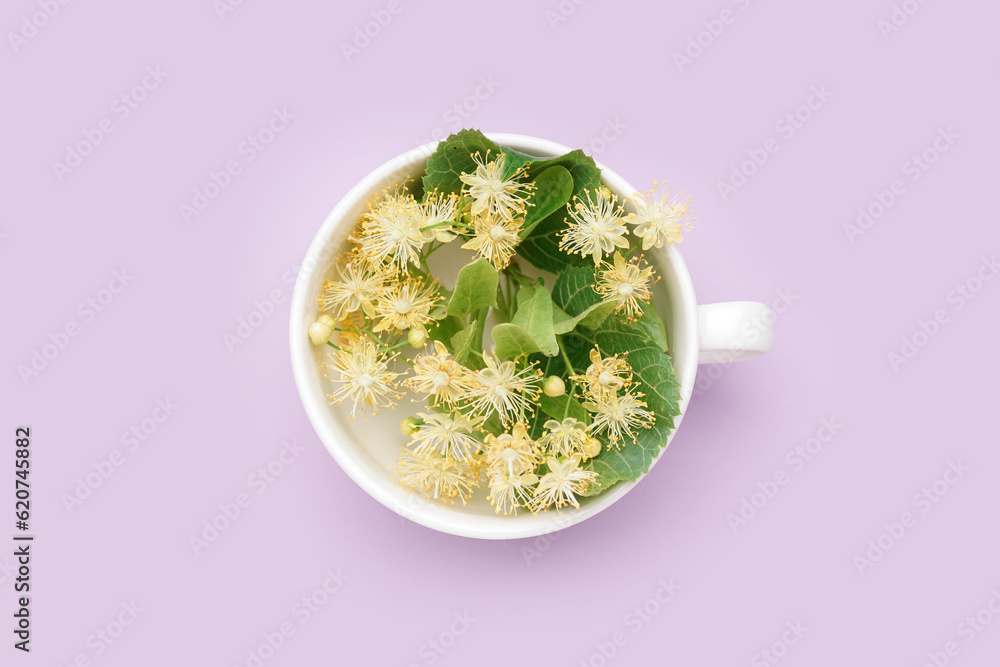 Cup with fresh linden flowers on lilac background