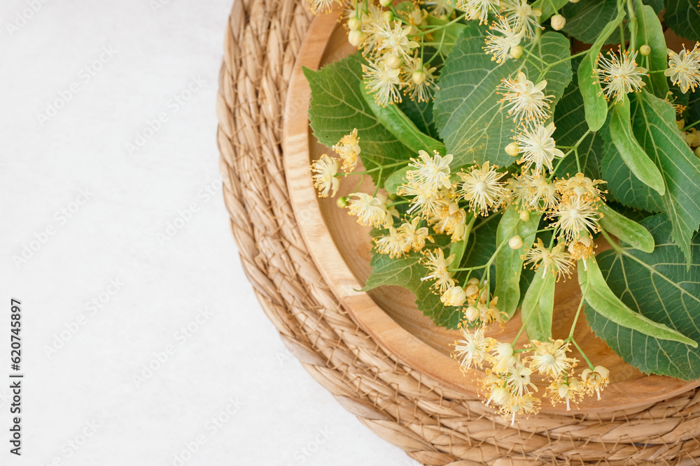 Wooden plate with branches of linden flowers on light background, closeup